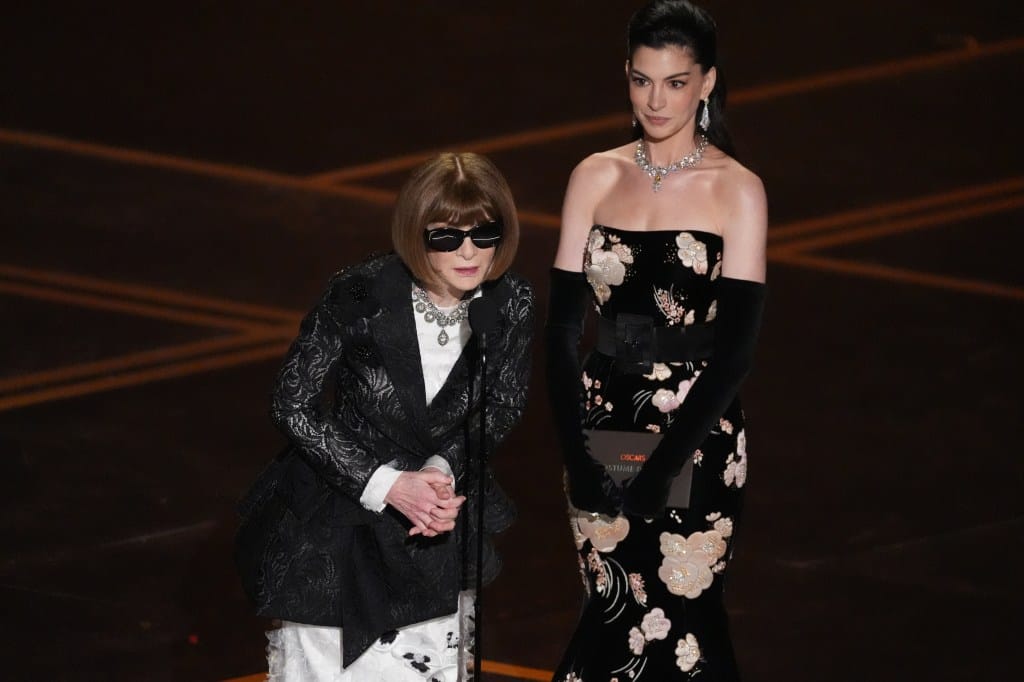 Anna Wintou, in a black lacy jacket over a white satin gown, and Anne Hathaway, in a black strapless floral gown and black gloves, present the award for best costume design at the Oscars.