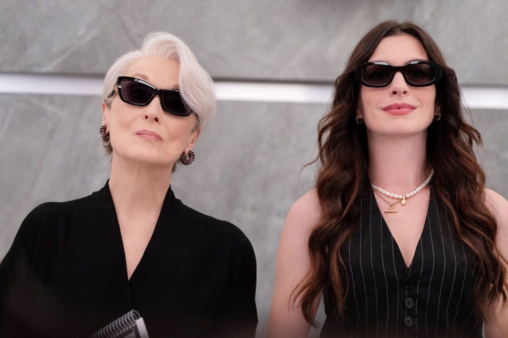 Meryl Streep, in a black jacket and sunglasses, and Anne Hathaway, in a black pinstriped waistcoat and sunglasses.