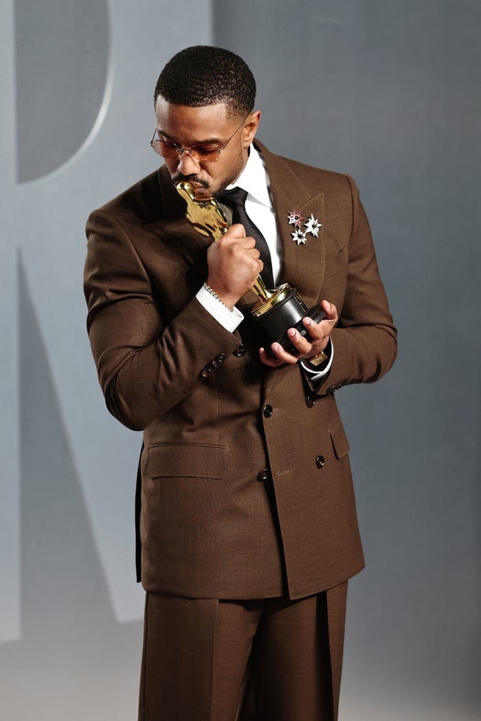 Person in a tailored suit holds an award, gazing at it