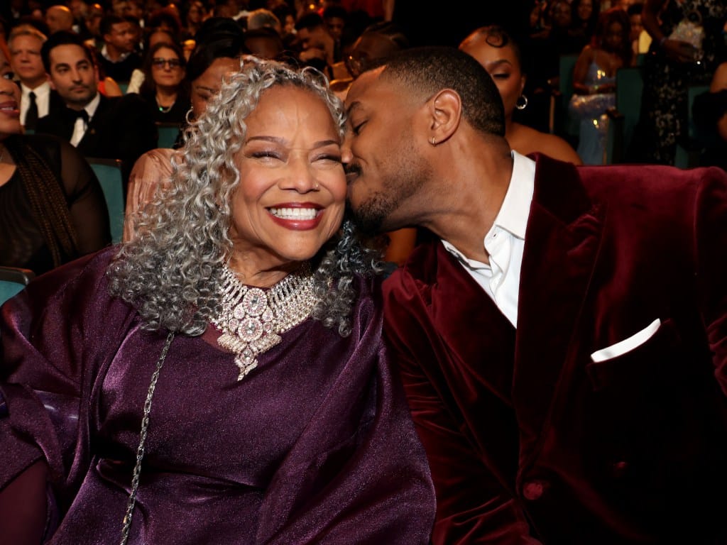 Michael B. Jordan, in a burgundy suit with white shirt, kissing Donna Jordan