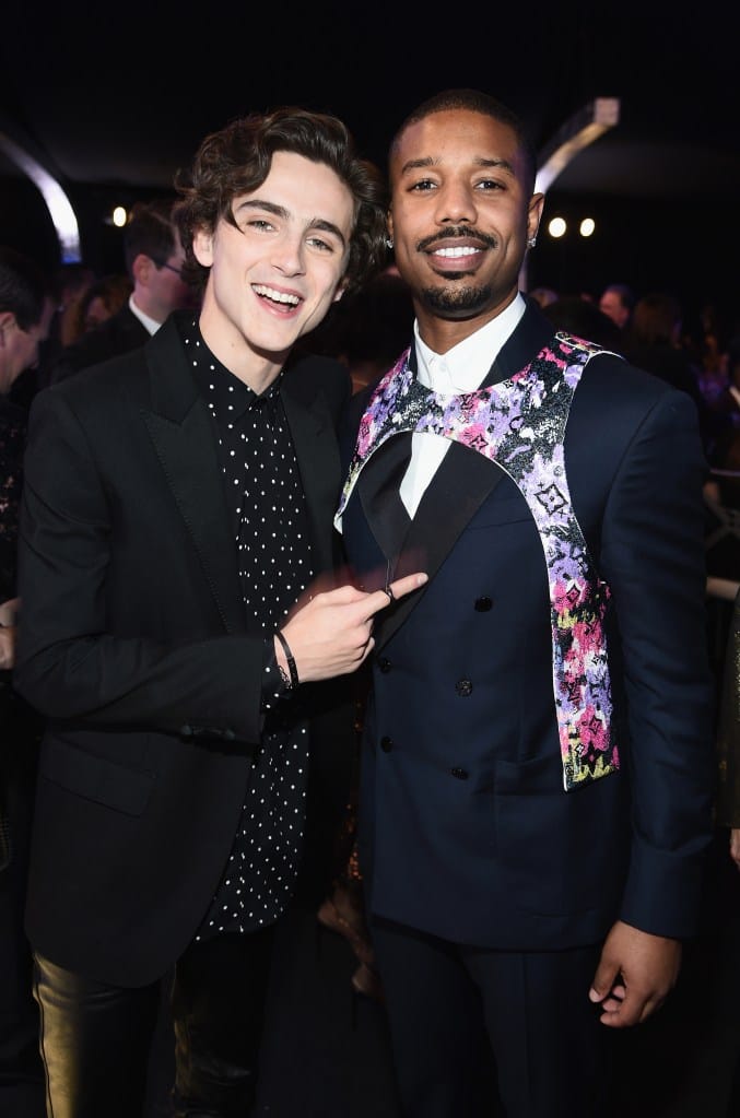 Timothée Chalamet, in a black jacket, black and white spotted shirt, pointing at Michael B. Jordan