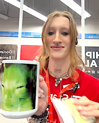 Person at a store holding a mug featuring a meme cat image, smiling, wearing casual attire with multiple accessories