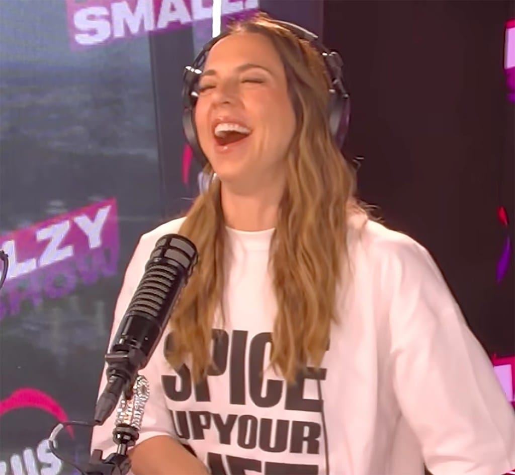Mel C. during an interview, wearing headphones and a white shirt with "SPICE UP YOUR LIFE" printed on it.